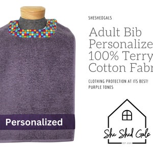 May include: Purple terry cloth adult bib with a colorful patterned trim and a personalized name tag. The bib is made of 100% terry cloth and cotton fabric. "She Shed Gals" is printed on the bottom right corner of the image.