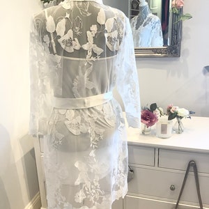 May include: White lace robe with floral embroidery and a satin sash. The robe is sheer and has a delicate, feminine look.