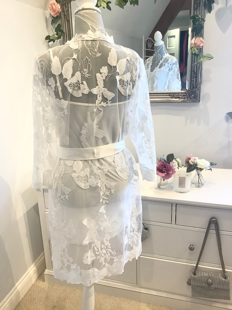 May include: White lace robe with floral embroidery and a satin sash. The robe is sheer and has a delicate, feminine look.