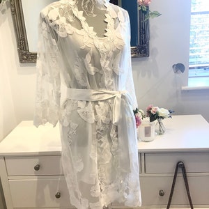 May include: White lace robe with long sleeves and a satin sash. The robe has a delicate floral pattern and is perfect for a bridal shower or wedding day.