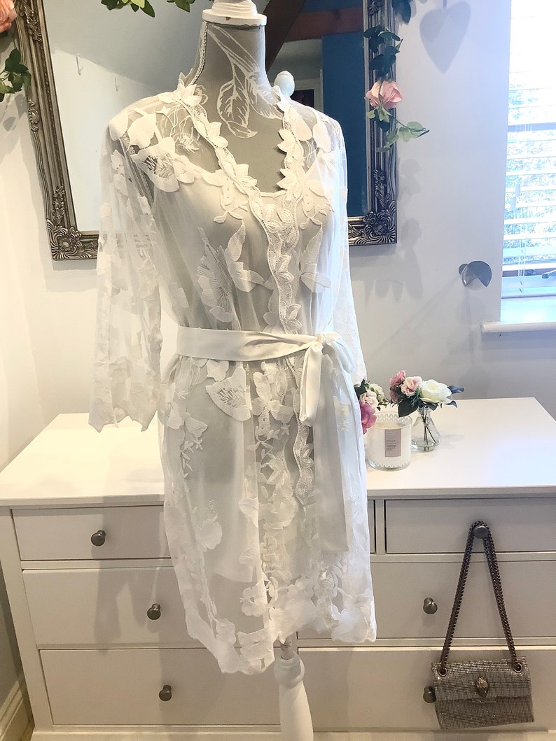 May include: White lace robe with long sleeves and a satin sash. The robe has a delicate floral pattern and is perfect for a bridal shower or wedding day.