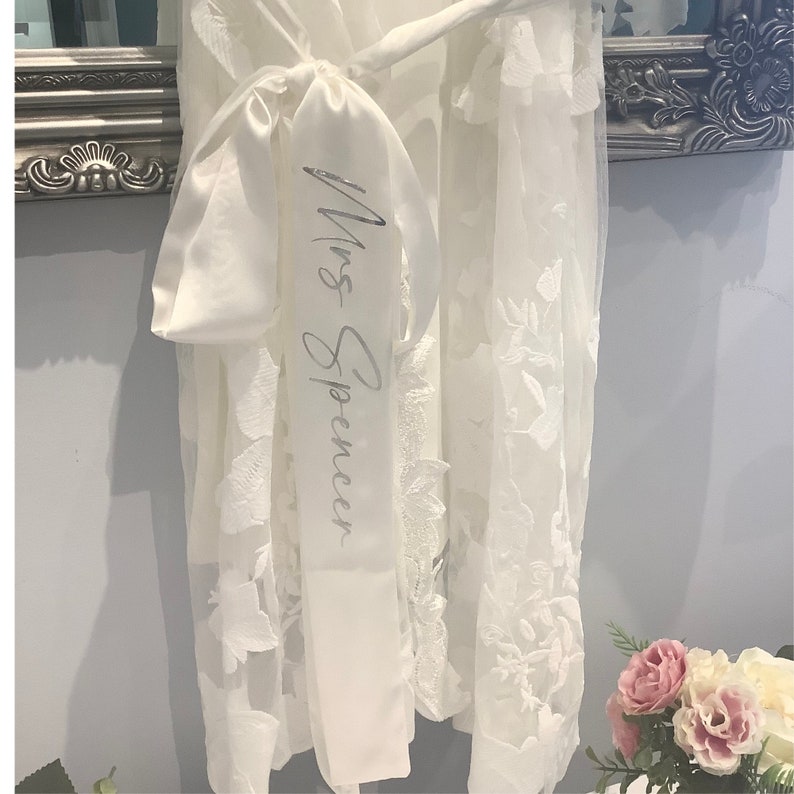 May include: White lace robe with a white satin sash that says "Mrs. Spencer" in silver lettering.