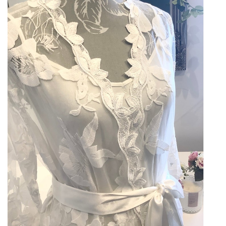 May include: White lace robe with a satin sash. The robe features a delicate floral pattern and a V-neckline.