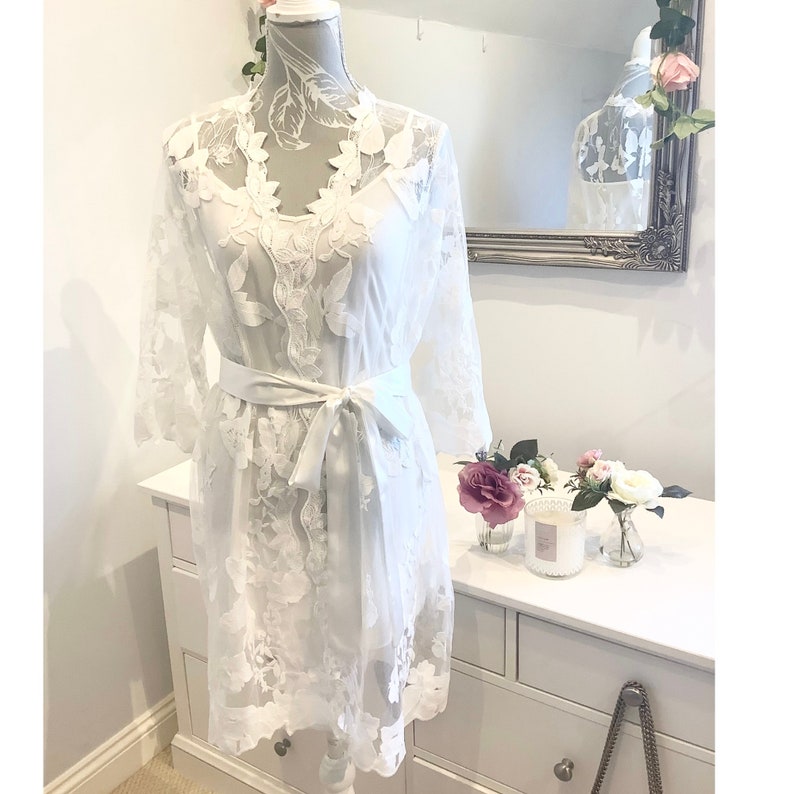 May include: White lace robe with long sleeves and a satin sash. The robe has a delicate floral pattern and is perfect for a bridal shower or wedding day.