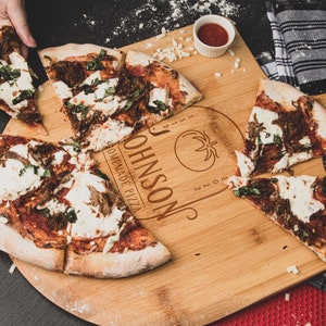 May include: A wooden pizza serving board with the text "JOHNSON'S HOMEMADE PIZZA" and a tomato graphic. The board is divided into sections and has a pizza slice in each section. The pizza has a red sauce base, mozzarella cheese, and green basil.