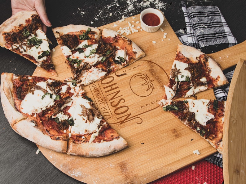 May include: A wooden pizza serving board with the text "JOHNSON'S HOMEMADE PIZZA" and a tomato graphic. The board is divided into sections and has a pizza slice in each section. The pizza has a red sauce base, mozzarella cheese, and green basil.
