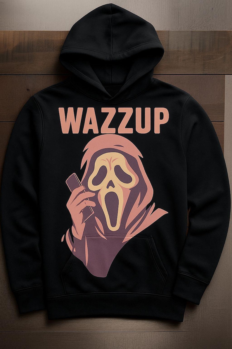 May include: Black hooded sweatshirt with the word "WAZZUP" in peach-colored letters. The graphic features a Scream mask holding a phone, in shades of peach, purple, and yellow. The sweatshirt has a front pocket and a drawstring hood.