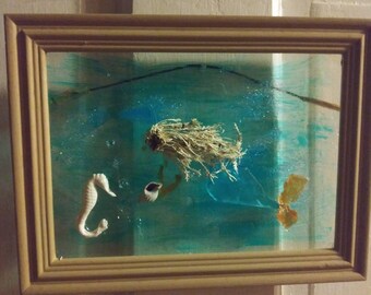 Può includere: Diorama incorniciato raffigurante una scena subacquea. Include un cavalluccio marino, una conchiglia e piante essiccate, su uno sfondo dipinto di blu e verde. La cornice è in legno marrone chiaro e la scena è racchiusa in vetro.