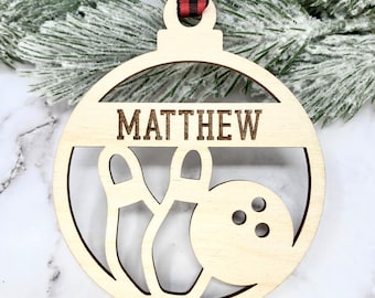 May include: A wooden Christmas ornament shaped like a bowling ball with two bowling pins inside. The ornament is personalized with the name "MATTHEW".
