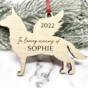 German Shepherd with angel wings memorial ornament. Ornament is made of wood with, “In loving memory of”, dog’s name, and year engraved on it. Ornament is hung with a red ribbon.