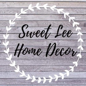 K&ouml;nnte beinhalten: Ein wei&szlig;er Kranz mit Bl&auml;ttern umgibt den Text "Sweet Lee Home Decor" auf einem grauen Holzgrund.