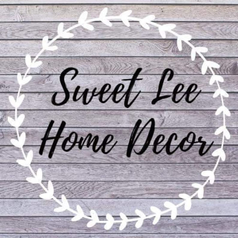 K&ouml;nnte beinhalten: Ein wei&szlig;er Kranz mit Bl&auml;ttern umgibt den Text "Sweet Lee Home Decor" auf einem grauen Holzgrund.
