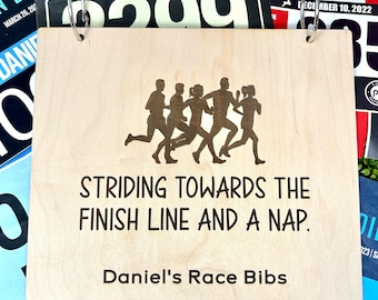 May include: A wooden sign with a silhouette of runners and the text "Striding towards the finish line and a nap. Daniel's Race Bibs".