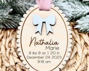 May include: A wooden oval ornament with a white bow, the name "Nathalia Marie", and the text "8 lbs 8 oz | 20 in December 24, 2023 8:18 am".