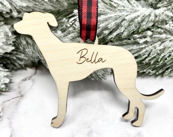 Op de afbeelding: Houten kerstversiering in de vorm van een windhond met de naam "Bella" erop gegraveerd. De versiering is bevestigd aan een rood-zwart geruit lint.