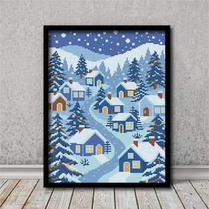 May include: Framed cross-stitch art depicting a winter village scene. The artwork features blue houses with snow-covered roofs, surrounded by evergreen trees and a winding road. The sky is a gradient of blue with falling snow.