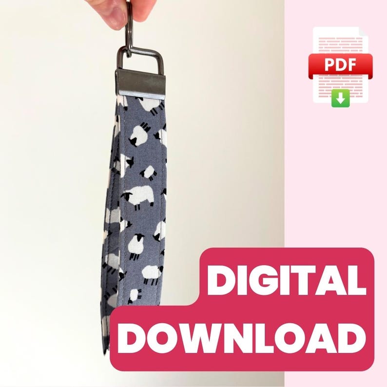 May include: A digital download PDF pattern for a sheep-themed key fob. The key fob is gray with white sheep printed on it. The key fob is attached to a silver key ring.