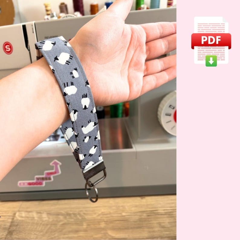 May include: A gray and white fabric key chain with a sheep pattern. The key chain has a metal ring and a metal clasp.