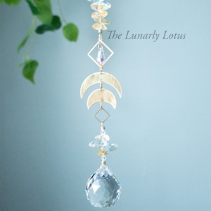 May include: A gold crystal suncatcher with a crystal ball at the bottom. The suncatcher features a geometric design with two crescent moons and a crystal in a square frame. The text "The Lunarly Lotus" is visible in the image.