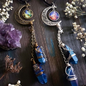 Puede incluir: Dos collares de plata en forma de media luna con cabujones de vidrio con tem&aacute;tica de galaxia. Cada collar presenta un cristal azul envuelto en alambre, colgando de una cadena con un dije de estrella.
