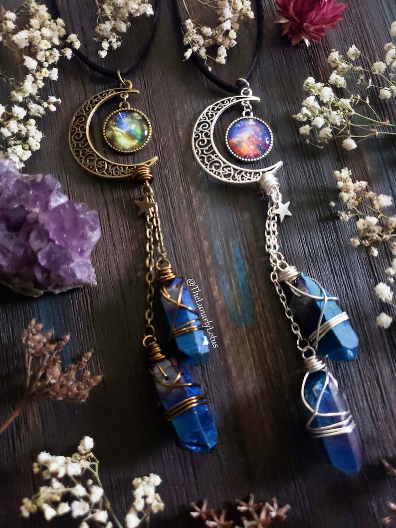 Puede incluir: Dos collares de plata en forma de media luna con cabujones de vidrio con tem&aacute;tica de galaxia. Cada collar presenta un cristal azul envuelto en alambre, colgando de una cadena con un dije de estrella.