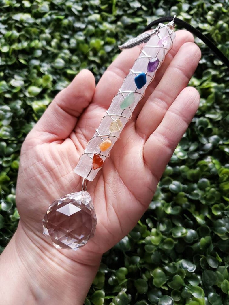 Puede incluir: Una varita de selenita blanca envuelta en alambre y adornada con siete piedras de chakra. Una bola de cristal transparente cuelga de la parte inferior de la varita.