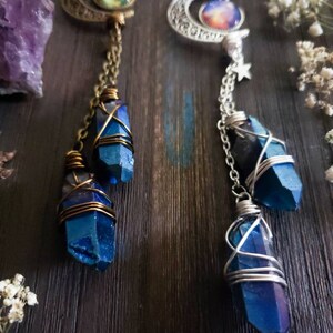 Puede incluir: Dos collares con colgantes de luna creciente y abalorios de cristal azul. Los abalorios est&aacute;n envueltos en alambre y cuelgan de cadenas. Los colgantes presentan im&aacute;genes con tem&aacute;tica de galaxias.