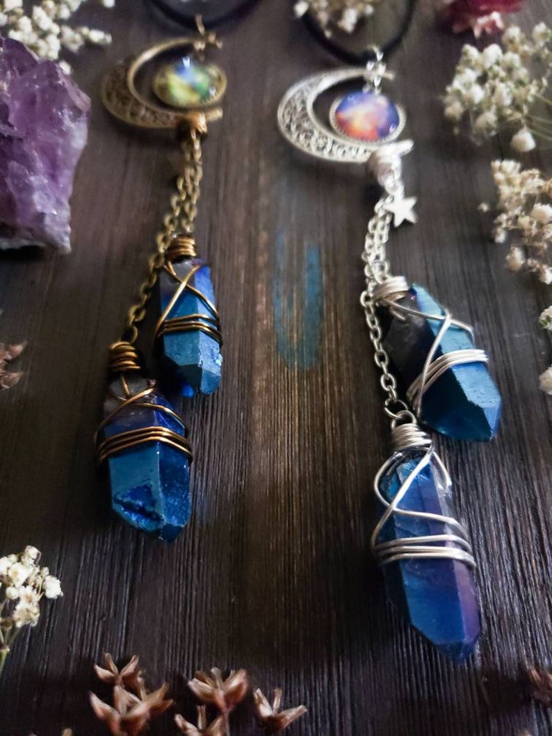 Puede incluir: Dos collares con colgantes de luna creciente y abalorios de cristal azul. Los abalorios est&aacute;n envueltos en alambre y cuelgan de cadenas. Los colgantes presentan im&aacute;genes con tem&aacute;tica de galaxias.