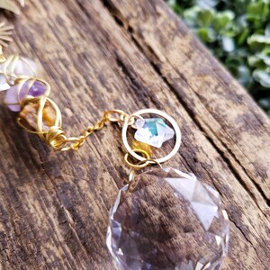 K&ouml;nnte beinhalten: Eine goldene Kette mit einer Kristallkugel und einem kleineren Kristallanh&auml;nger, die daran h&auml;ngen. Die Kette ist um ein St&uuml;ck Holz gewickelt.