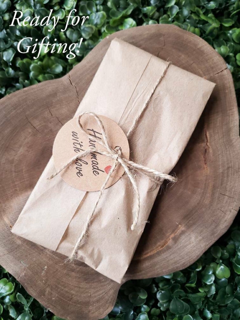 K&ouml;nnte beinhalten: Ein braunes Papierpaket, das mit Schnur gebunden ist und einen runden Anh&auml;nger mit der Aufschrift "Handgefertigt mit Liebe" tr&auml;gt. Das Paket liegt auf einer Holzoberfl&auml;che.