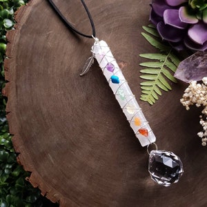 Puede incluir: Una varita de cristal blanco con siete piedras de chakra envueltas en alambre, un amuleto de pluma de plata y un colgante de cristal transparente que cuelga de un cord&oacute;n negro.