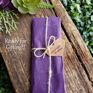May include: A purple gift bag tied with twine and a brown heart-shaped tag that says "Handmade with love".