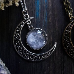 May include: A silver crescent moon pendant necklace with a glass cabochon featuring a black and white moon image.