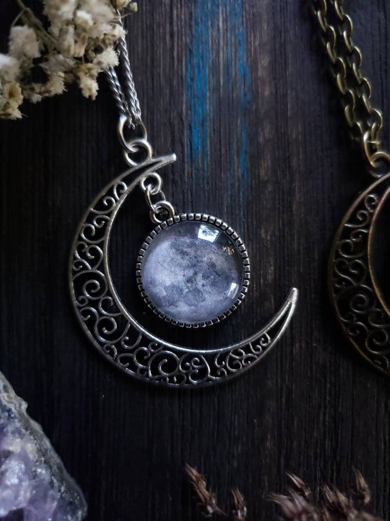 May include: A silver crescent moon pendant necklace with a glass cabochon featuring a black and white moon image.