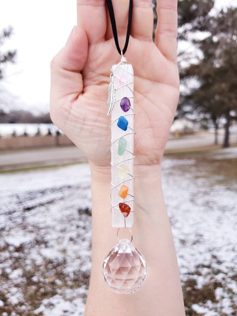 Puede incluir: Una varita de selenita blanca con una punta de cristal en la parte inferior. La varita est&aacute; envuelta con alambre y tiene siete piedras de chakra unidas. Las piedras son rosa, p&uacute;rpura, azul, verde, amarilla, naranja y roja. La varita cuelga de un cord&oacute;n negro.