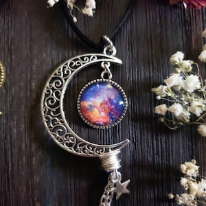 Puede incluir: Un collar de plata en forma de media luna con un colgante de vidrio con tem&aacute;tica de galaxia y un dije de estrella en una cadena.