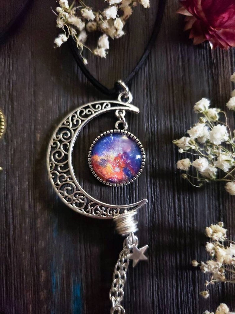 Puede incluir: Un collar de plata en forma de media luna con un colgante de vidrio con tem&aacute;tica de galaxia y un dije de estrella en una cadena.