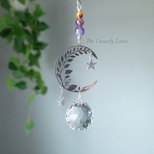 May include: A silver crescent moon charm necklace with a crystal ball pendant and small star charms. The necklace features a leafy design on the moon and has a silver chain with amethyst, tiger's eye, and clear beads.