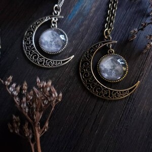 May include: Two silver and bronze necklaces with crescent moon pendants featuring a detailed filigree design and a round glass moon charm.