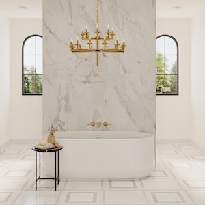 Puede incluir: Una bañera blanca con grifería dorada se encuentra en un baño con paredes de mármol blanco y una lámpara de araña dorada. El baño tiene suelos de baldosas blancas con un patrón geométrico.