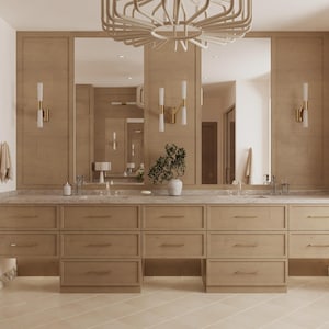 Può includere: Un mobile da bagno moderno con finitura in legno chiaro, con più cassetti e un piano in marmo. Il mobile è affiancato da grandi specchi e applique, con un apparecchio di illuminazione decorativo sopra. Una pianta e oggetti decorativi completano l'insieme.