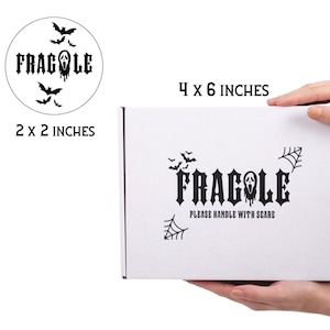 May include: A white box with black Halloween-themed graphics and text. The box is labeled "FRAGILE" with a ghost face and bats. The text "PLEASE HANDLE WITH SCARE" is also present. The box measures 4 x 6 inches.