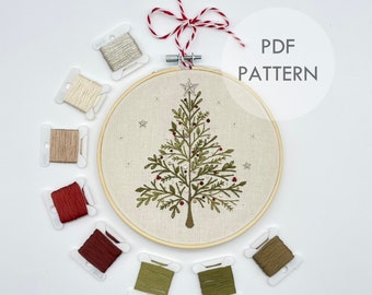 May include: Embroidery pattern for a Christmas tree with red berries and a star on top. The pattern is displayed in a wooden embroidery hoop with a variety of floss colors surrounding it. The text "PDF PATTERN" is displayed in a white circle.