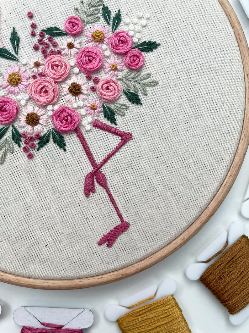 May include: Embroidered hoop art featuring a pink flamingo with a bouquet of pink and white flowers. The hoop is made of wood and has a natural finish.