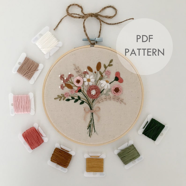 以下が含まれることがあります： 木製の刺繍枠に、ピンク、白、緑の花が咲いた花束の刺繍のPDFパターンです。パターンには、茶色、ピンク、白、緑、黄色の糸など、さまざまな糸の色が含まれています。