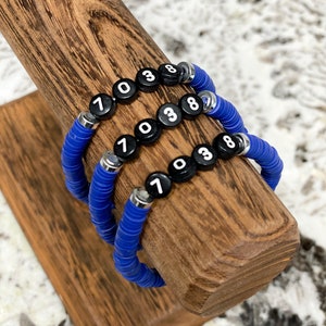 May include: Three blue beaded bracelets with black beads that have white numbers on them. The numbers on the beads are 7, 0, 3, and 8.