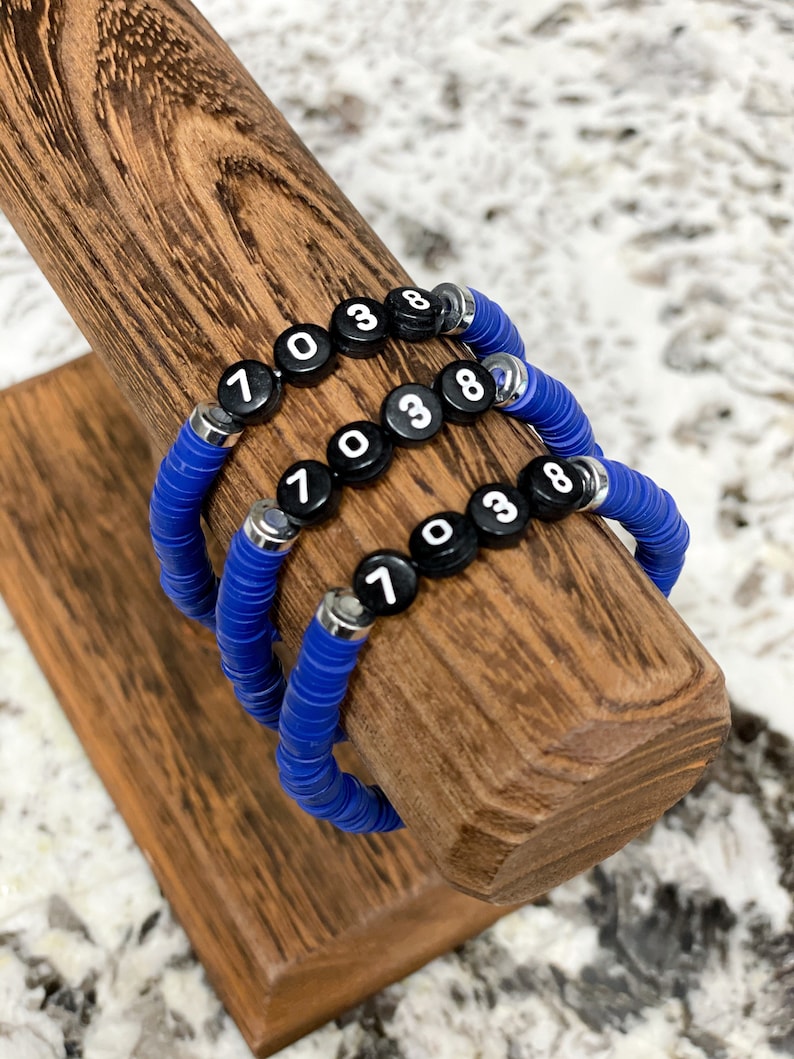May include: Three blue beaded bracelets with black beads that have white numbers on them. The numbers on the beads are 7, 0, 3, and 8.