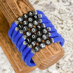 May include: A stack of blue silicone bracelets with black and white number charms. The numbers on the charms are 9, 2, 4, 0, 4, 9, 1, 2, 4, 0, 3, 5, 7, 8, 0, 9, 5, 0, 1, 3, 5, 2.