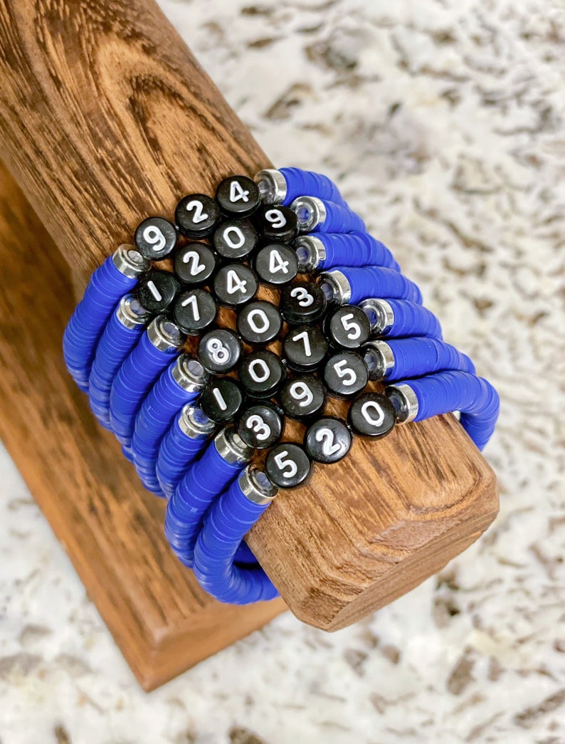 May include: A stack of blue silicone bracelets with black and white number charms. The numbers on the charms are 9, 2, 4, 0, 4, 9, 1, 2, 4, 0, 3, 5, 7, 8, 0, 9, 5, 0, 1, 3, 5, 2.