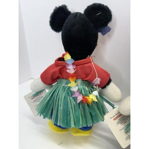 Puede incluir: Mu&ntilde;eco de peluche de Mickey Mouse con una camisa roja, una falda de hierba verde y un lei colorido. El mu&ntilde;eco tiene orejas negras, guantes blancos y zapatos amarillos. El mu&ntilde;eco tiene una etiqueta.